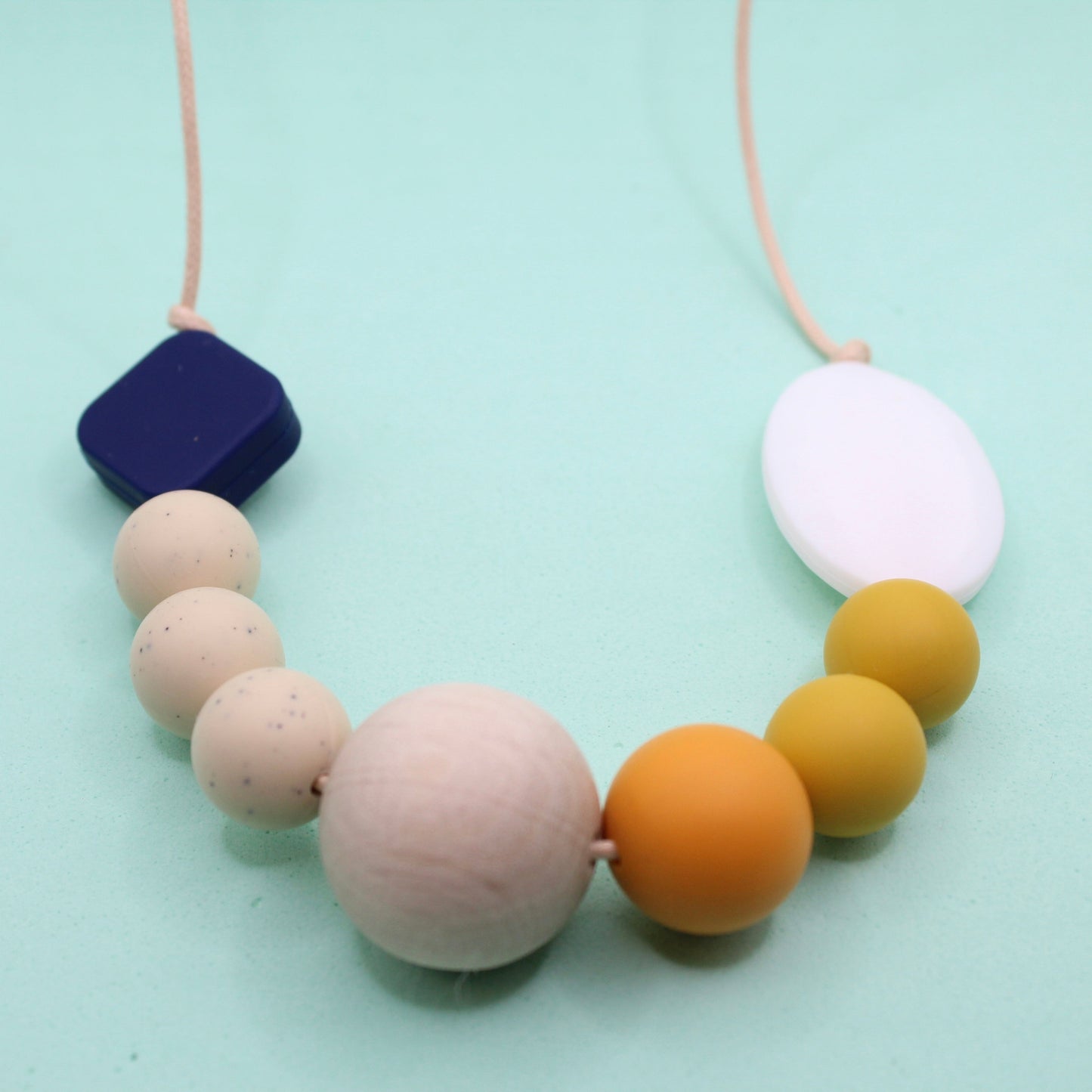 Navy and mustard silicone beaded necklace with speckled cream, mango, and natural wood beads on a light background.