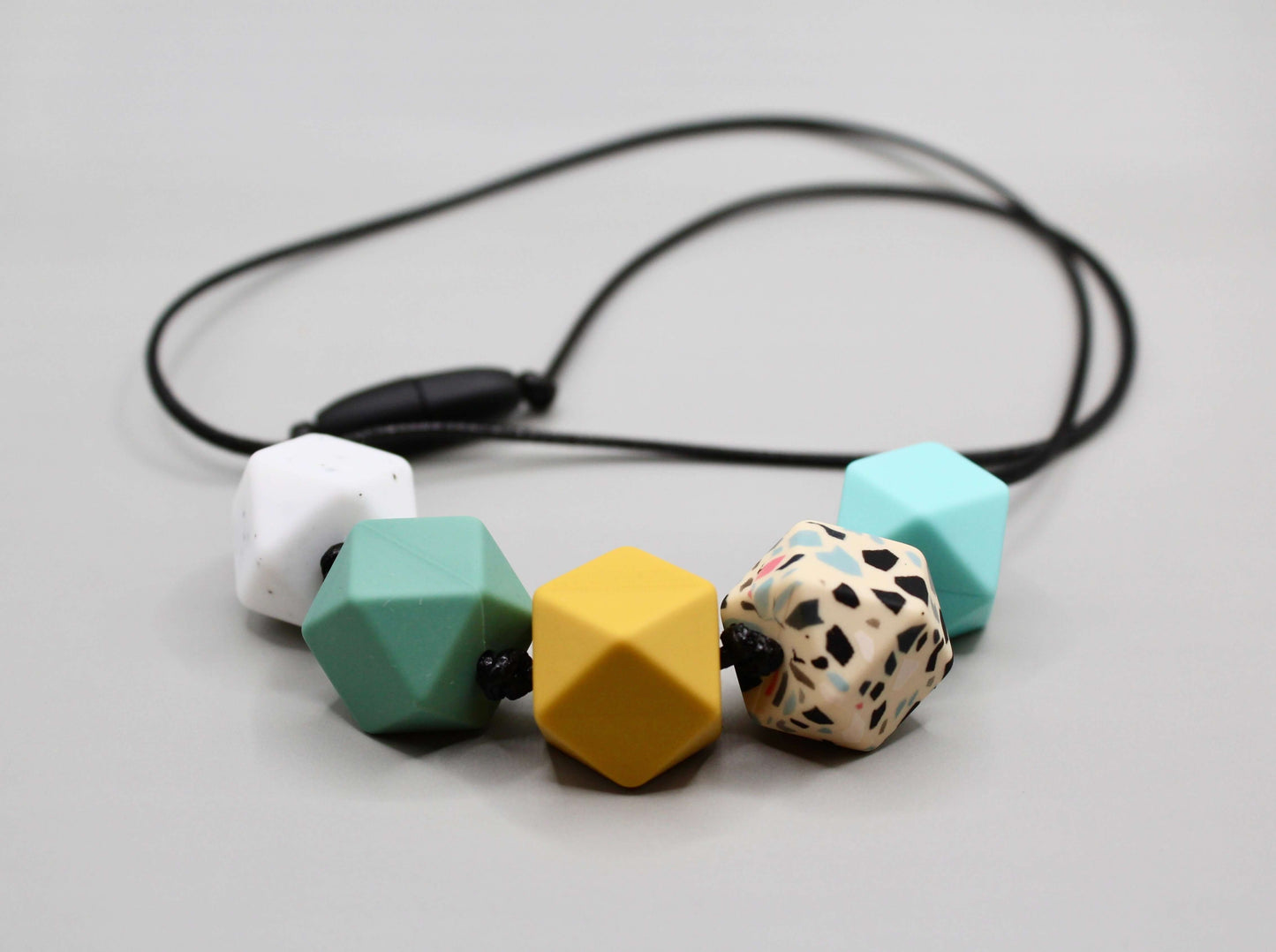 Hexagon silicone necklace with 17mm beads in white, green, yellow, and speckled colors on black cord, sensory-friendly and customizable.
