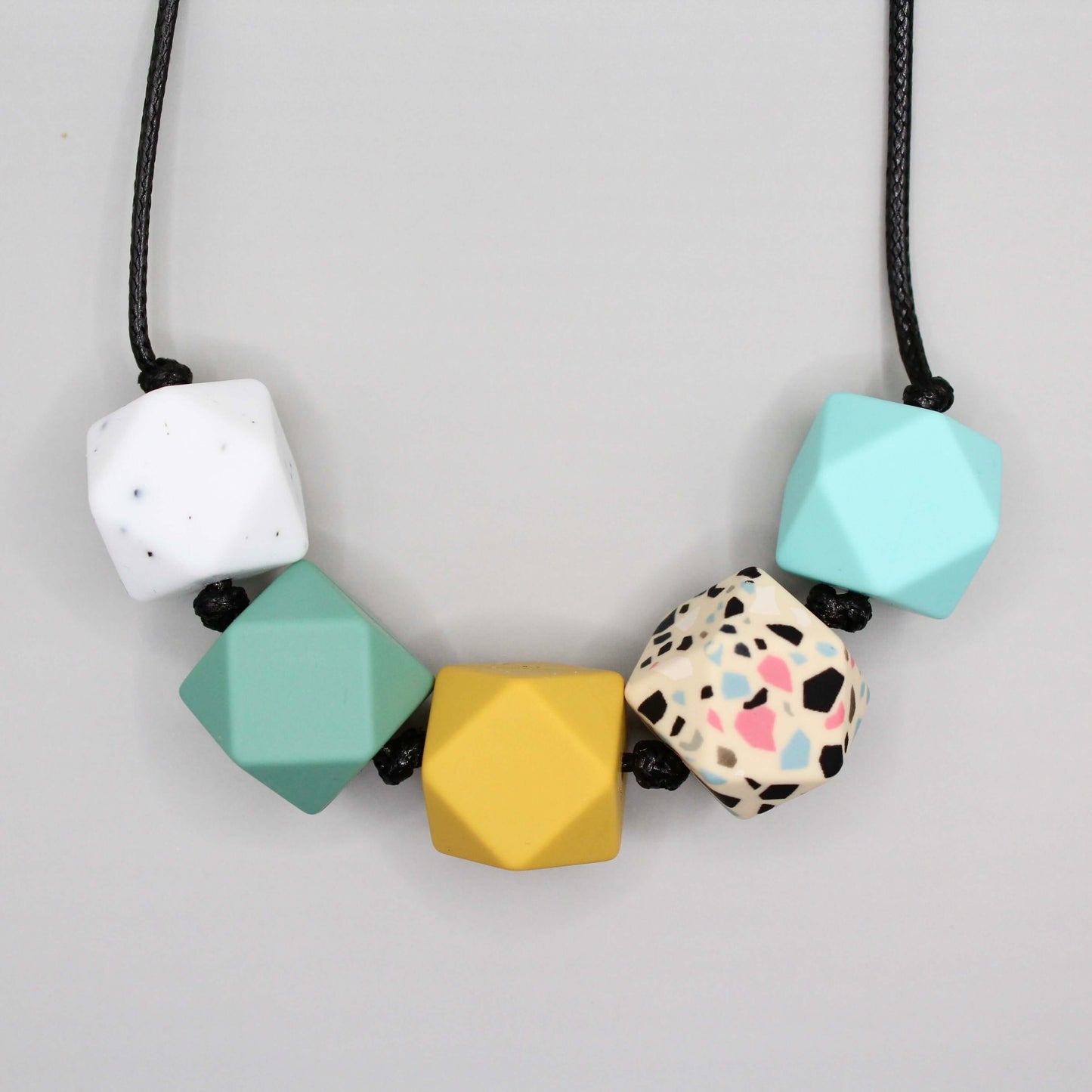 Hexagon silicone necklace with baby-friendly sensory beads in white, green, yellow, multicolored, and blue on a black cord.