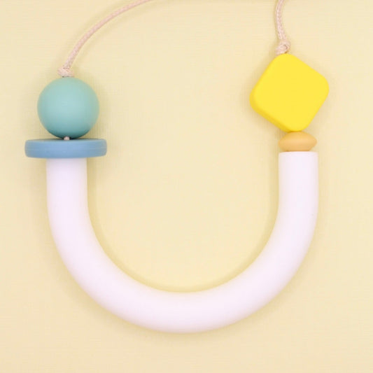 White U shape silicone asymmetrical necklace photographed laying flat from above on a contrasting lemon yellow background.