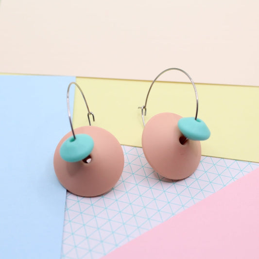 Silicone hoop dangle earrings in Peachy Pink. 30mm Handmade stainless steel hoops. Photographed against a mixed pastel paper bakcground.