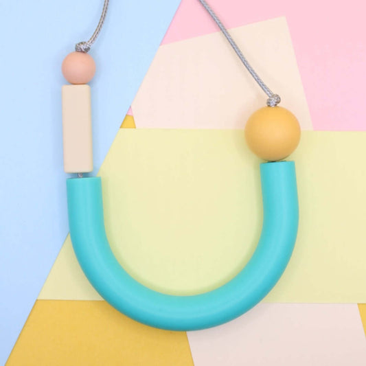 Turquoise U shaped silicone necklace photographed laying flat from above against mixed pastel paper background.