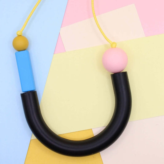 Black U shaped silicone necklace photographed laying flat from above against mixed pastel paper background.