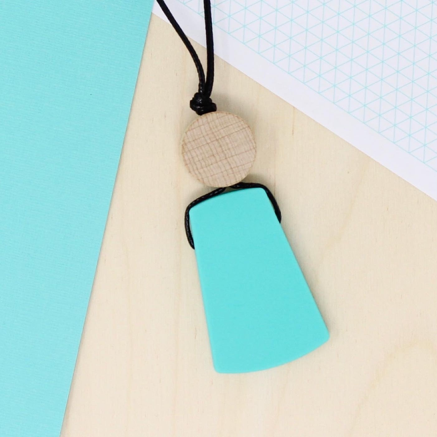 Turquoise trapezoid shaped silicone pendant necklace laying flat and photographed from above on a turquoise and natural wood background.